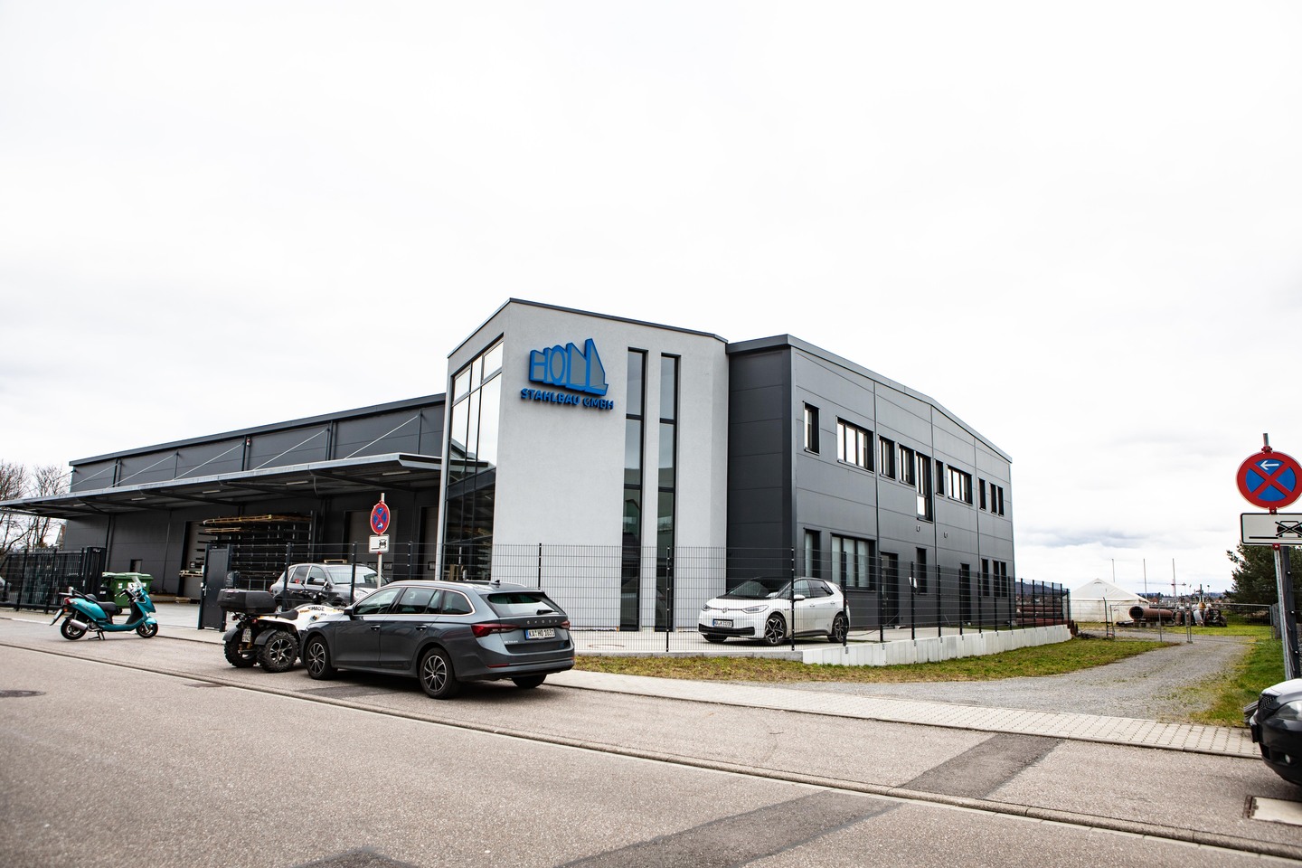 Ein modernes Bürogebäude mit dem Logo "HOM" und geparkten Autos im Vordergrund.