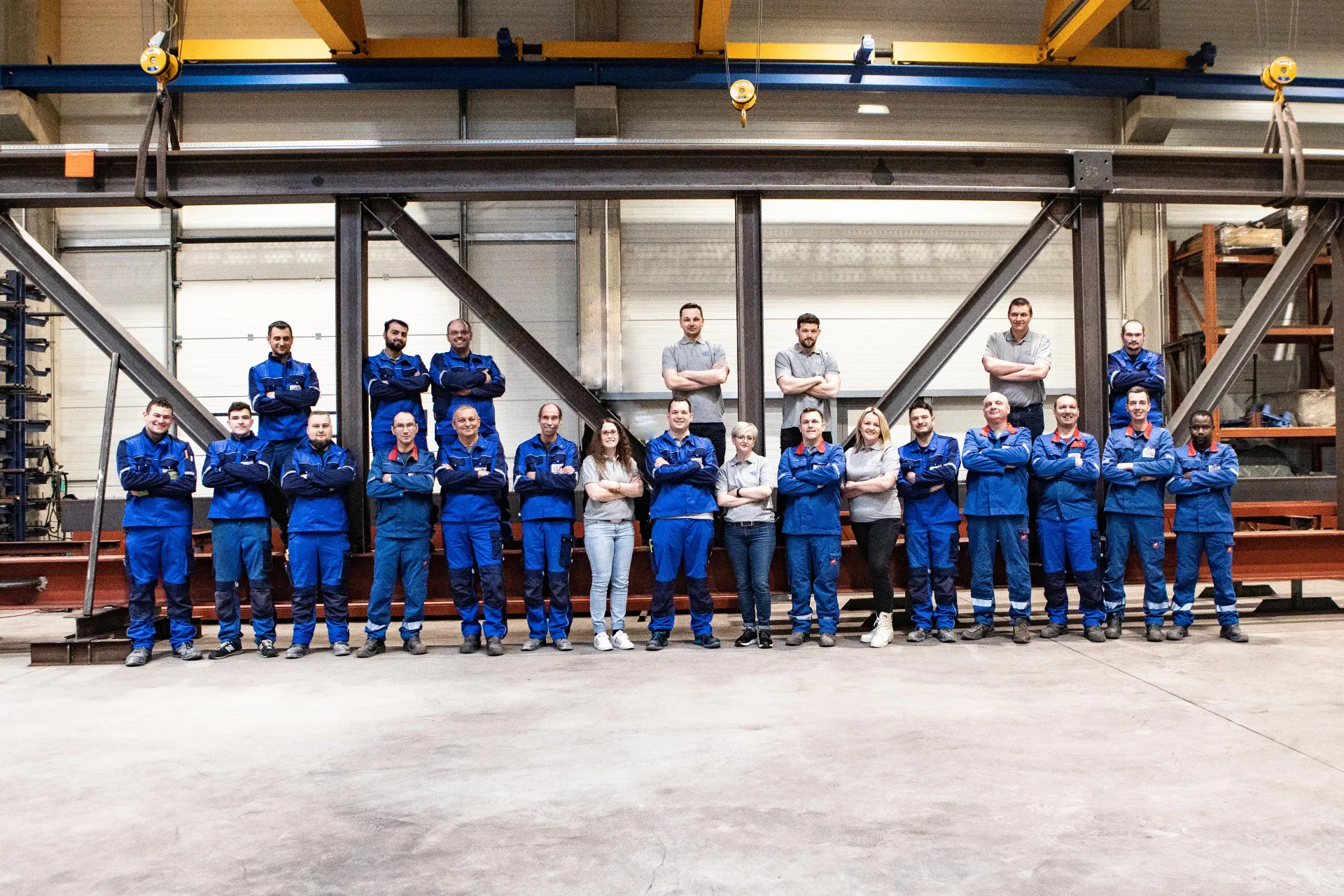 Gruppe von Menschen in blauen Arbeitsanzügen steht in einer Fabrikhalle und posiert für ein Gruppenfoto.