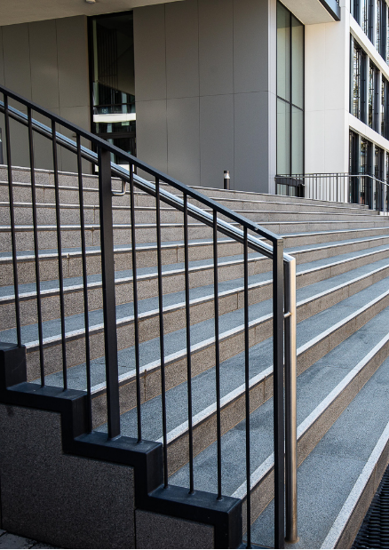 Eine Treppe mit grauen Stufen und schwarzen Metallgeländern führt zu einem modernen Gebäude.