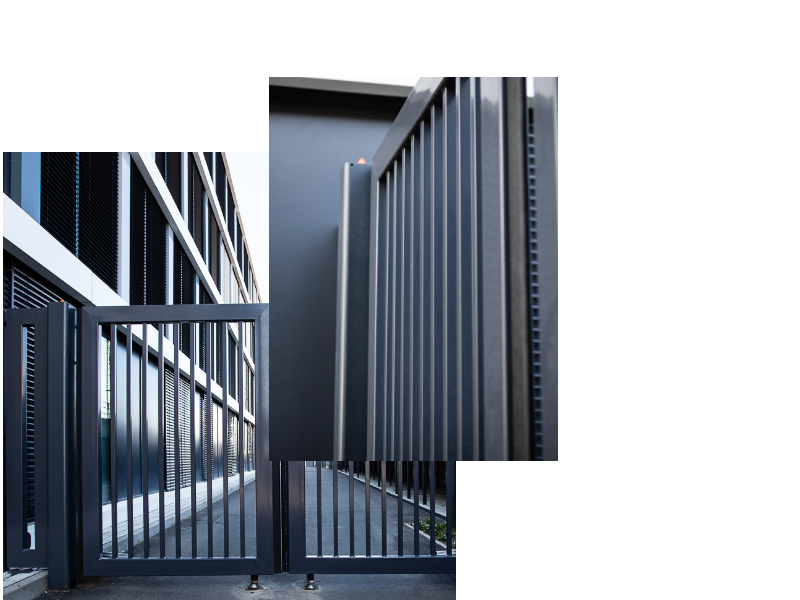 Ein modernes Metalltor führt zu einem gepflasterten Weg vor einem Gebäude mit großen Fenstern.